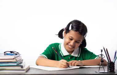 Çok güzel bir Hintli kız öğrenci, beyaz arka planda çalışma masasında yazıyor.