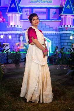 Batı Bangal 'da festival gecesi puja pandalının önünde gülümseyen geleneksel sari elbiseli Hintli bir kadın.