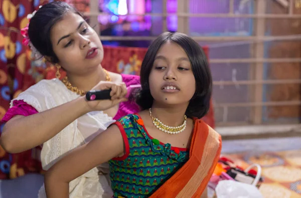 An Indian mother helping her girl child in traditional dress to comb hair indoors at a festival night