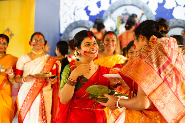 Birbhum, West Bengal, India - October 24th 2023: A beautiful woman in traditional dress with red colored smiling face playing with sindoor during last day of Durga Puja