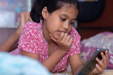 Yatakta cep telefonu kullanan güzel bir Hintli kız çocuğu.