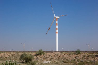 Elektrik üretmek için açık mavi arka planda duran kırmızı ve beyaza boyanmış rüzgar değirmenlerinin sayısı