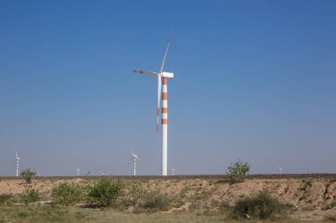 Elektrik üretmek için açık mavi arka planda duran kırmızı ve beyaza boyanmış rüzgar değirmenlerinin sayısı