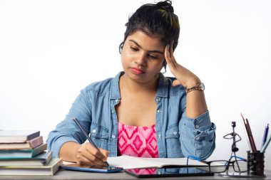 Güzel bir Hintli üniversite öğrencisi çalışma masasında ve beyaz arka planda okuyor ve yazıyor.