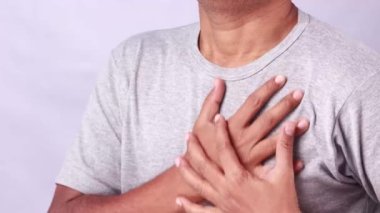 Acı için göğsünü tutan bir Hintli beyaz arka planda acı dolu bir ifade sergiliyor.