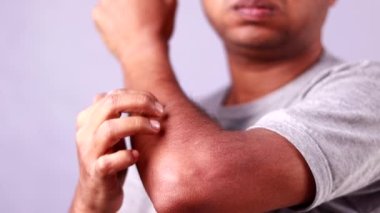 Tenis oynamak için dirseğini tutan Hintli bir adam beyaz arka planda acı veren bir ifade sergiliyor.