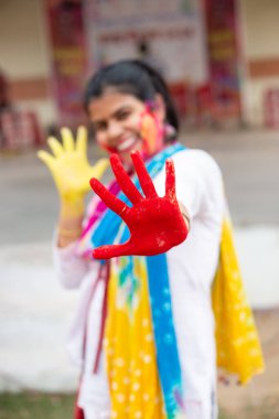 Holi pozları sırasında beyaz elbiseli ve pudra boyalı renkli yüzlü Hintli bir Bengalli kadın renkli ellerle poz veriyor.