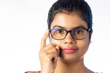 Siyah çerçeveli gözlük takan ve beyaz arka planda kameraya bakan güzel bir Hintli kadının portresi.