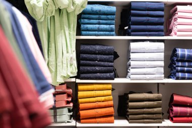 Renkli pamuk gömleklerin üst üste dizildiği bir alışveriş merkezinin rafları.