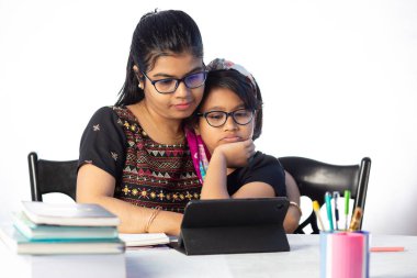 Beyaz arka planda annesinin yanı sıra tabletle çalışan Hintli bir kız öğrenci.
