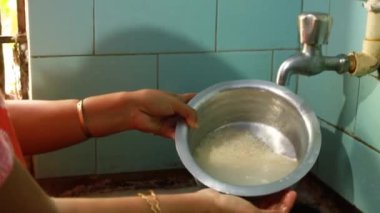 Hindistan mutfağındaki musluğun altında pirinç tanelerini durulamak için alüminyum kap kullanılıyor.