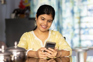 Sarı elbiseli güzel bir Hintli kadın masa başında oturmuş gülümsüyor.