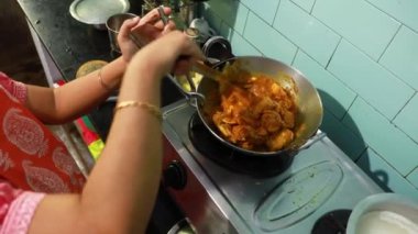 Hintli bir ev hanımı mutfakta yemek önlüğü giyip gaz fırınındaki alüminyum çatallarda köri pişiriyor.