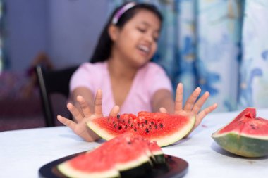 An Indian girl showing dislike gesture for eating water melon indoors clipart