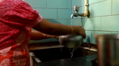 Hintli bir ev kadını mutfakta musluğun altında bulaşık yıkıyor.