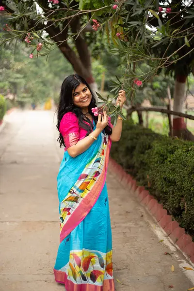 Stock image A pretty beautiful Indian Bengali woman in traditional wear saree posing with pink flower outdoors smiling face