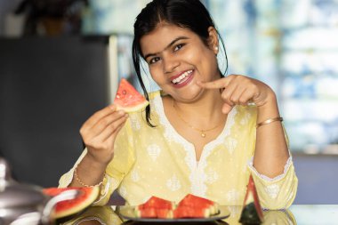 Sarı elbiseli güzel bir Hintli kadın. Kapalı alanda gülen yüzlü kırmızı karpuz yiyor.