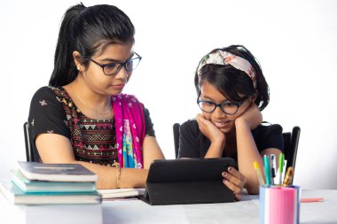 Beyaz arka planda annesinin yanı sıra tabletle çalışan Hintli bir kız öğrenci.