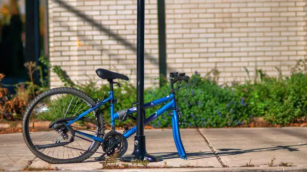 The blue bicycle is locked at the pole on the sidewalk. The front wheel was stolen from the thief.