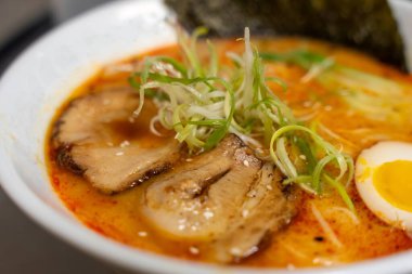 This image showcases a Spicy Tonkotsu ramen bowl of traditional Japanese ramen with slices of pork, halved boiled egg, seaweed, green onions, and other toppings, served in a white bowl. clipart