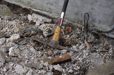 A worn pickaxe rests against a concrete wall, surrounded by rubble and debris. This scene captures the raw essence of construction and excavation work, showcasing tools of the trade in action. clipart