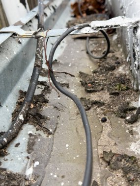 Açık hava elektrik kablolarının yakın görüntüsü bozulmuş metal olukların arasında aşınma ve hasar izleri gösteriyor..