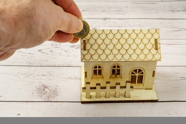 Miniature wooden house and hand introduced euro coin. Savings concept for house purchase. Rise in mortgage interest rates