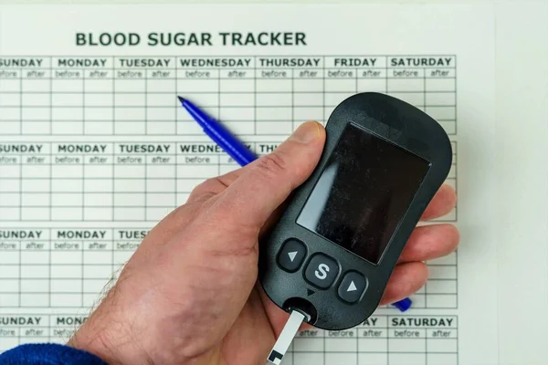Hand holding a glucometer to determine the level of sugar in the blood. Concept of high blood glucose level. Table for recording blood sugar levels
