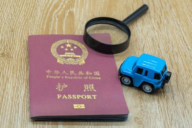 Tahta bir masada Çin Halk Cumhuriyeti pasaportu. Minyatür araba ve büyüteç. İş gezisi ve tatil konsepti
