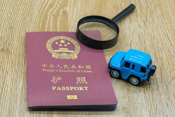 Passport of the People's Republic of China on a wooden table. Miniature car and magnifying glass. Business trip and holiday concept
