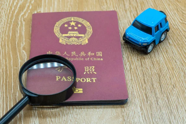 Passport of the People's Republic of China on a wooden table. Miniature car and magnifying glass. Business trip and holiday concept