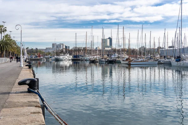 stock image Barcelona, Spain-April 12, 2023. A tranquil scene of a sailboats gliding in the harbor with reflections on the still water, surrounded by Barcelona port vell and its nautical vessels