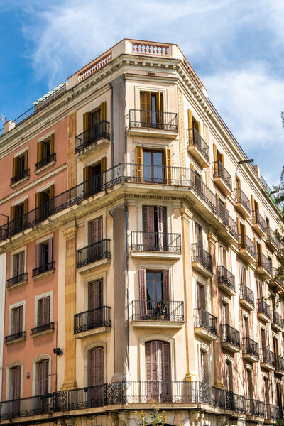 Apartment complex in Barcelona, Spain. Beautiful art nouveau building, with its striking facade and surrounding residential neighborhood. The bright blue sky highlights the majestic tower against the clouds.