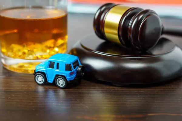 Judge\'s mace on a table in a court of law, glass of whiskey and miniature car. No drinking while driving concept