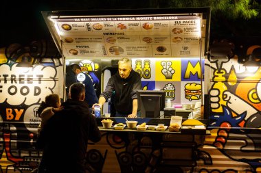 Barcelona, Spain-November 25, 2023. Group of people having fun while eating in front of a truck modified for mobile fast food service. Food truck clipart