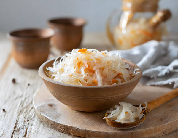 bowl of sauerkraut on a wooden board, with a fork and pottery in the background, showcasing a rustic and appetizing setting.