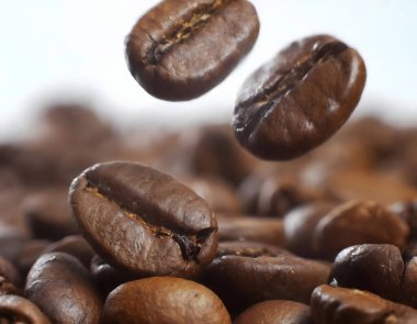 Close-up of coffee beans falling into a pile of coffee beans on a white background with varying shapes and sizes, and intense brown colour, falling in slow motion and forming a small heap clipart