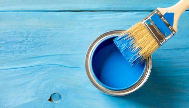 Mavi bir boya kutusu yanında boya fırçası olan ahşap bir yüzeye oturur. Mavi boya resim için kullanılmaya hazır.