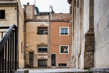 Bulutlu bir gökyüzü altında mimari dokular ve desenler gösteren eski binalar arasındaki dar görünüm, Badalona, İspanya