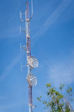 Telekomünikasyon kulesi. Güneşli bir günde çeşitli antenleri ve şanzıman çanaklarını destekleyen uzun metal bir yapı.