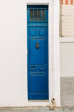 Canlı bir mavi vintage kapı, desenli beyaz bir duvara karşı duruyor, tarih ve tasarım hissi uyandırıyor..