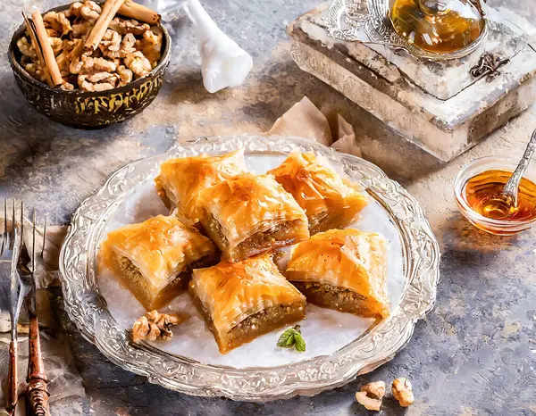 Geleneksel tatlı baklavası, kırsal bir masada, içinde malzemeler ve çatal bıçaklar olan cam bir tabakta servis edilir..