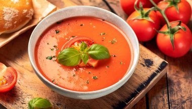 Bir kase geleneksel İspanyol gazpacho otlarla süslenmiş, ahşap bir masada kırsal bir kasede servis ediliyor..