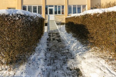 Binanın girişinde, engelliler için kışın tırabzanları olan metal bir rampa var.