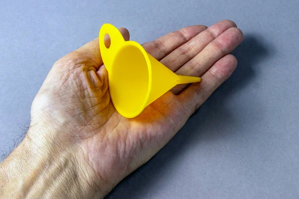 Yellow mini portable plastic funnel in palm of hand close up on gray background