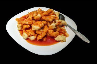 Fried chicken pieces with crispy crust and sauce on a white plate on a black background isolated
