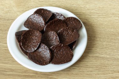 Dark chocolate chips with puffed rice in a white plate on an oak table surface