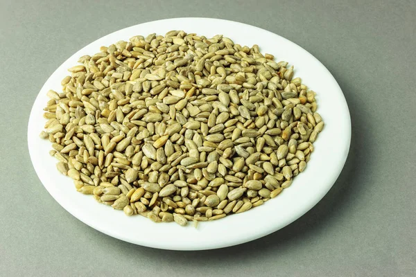 stock image Heap of sunflower seeds without shell in white plate on gray background top view