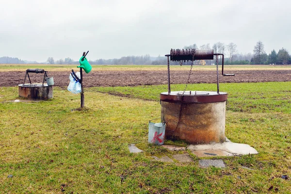 stock image Two old wells with metal lid and roller, buckets for collecting water and watering can in the village in spring