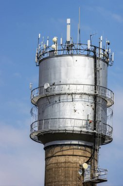 Güneşli bir günde arka planda gökyüzü olan eski bir su kulesindeki birçok farklı iletişim antenleri